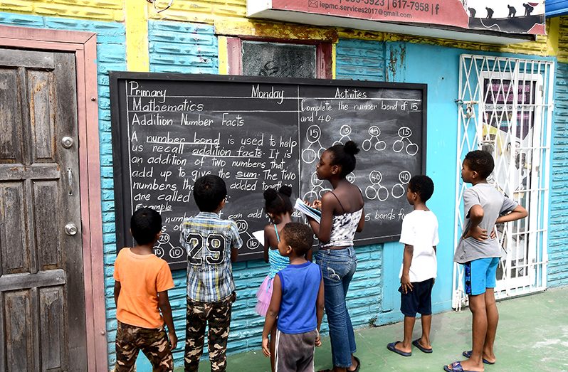 Nine year old Roshana Pickett (third from right) and 11-year-old Nicholas Martin (second from left) were among a number of children who took interest and copied work from this chalkboard set up outside of the Assembly of God church on Durban Street, Georgetown. (Adrian Narine photo)