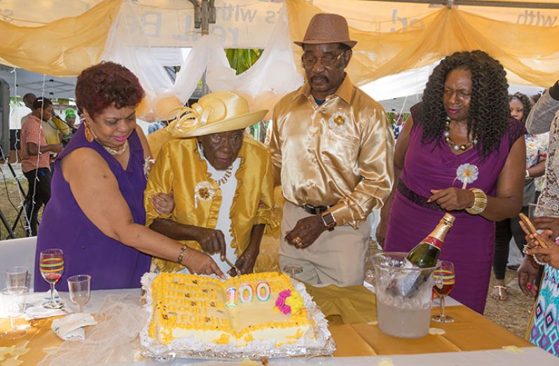Minister of Social Protection, Amna Ally (left), is seen sticking the cake with Iris John at her 100th birthday celebration, while John’s adopted son, Felix Nestor and Regional Chairman of the Demerara-Mahaica Region, Genevieve Alleyne, look on.  [Delano Williams photo]