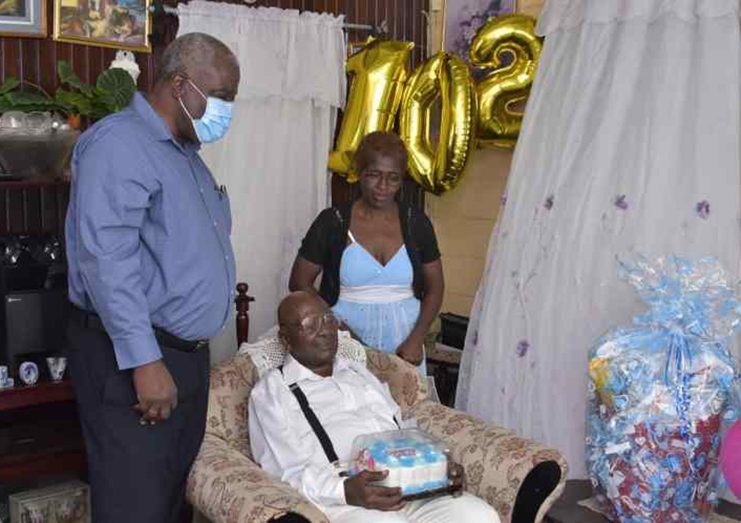 Guyana’s oldest surviving war veteran, Mr. Benjamin Durant (seated) celebrated his 102nd birth anniversary on Sunday at his Goedverwagting, East Coast Demerara (ECD) home with his relatives and Prime Minister, Brigadier (ret’d) Mark Phillips (left) (DPI photo)