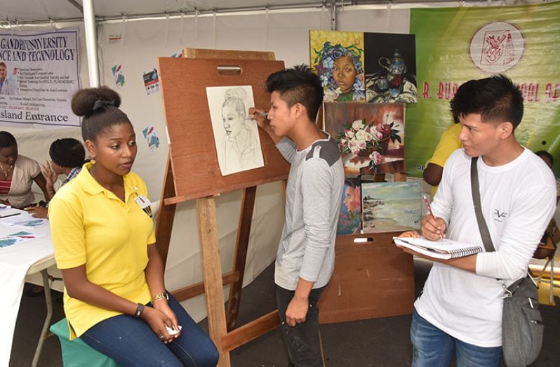 Students of the E.R Burrowes School of Art, Jude Bartholomew (right) and Ransford Simon (middle) sketch portraits of their subject, Renella Hamlet, at yesterday’s Youth Exposition and Health Fair