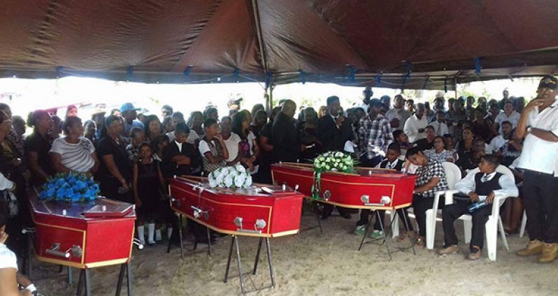 The three caskets bearing the remains of the men found dead aback Black Bush Polder last Friday are seen  at the home of the Chandradeos at Mibicuri, where hundreds gathered for the funeral. Mrs Chandradeo, who lost her husband, 15-year-old son and brother is seen seated between her younger sons