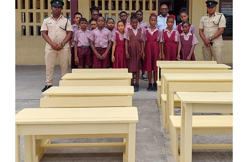 Prison officers and pupils of Timehri Primary School with the desks and benches made by inmates