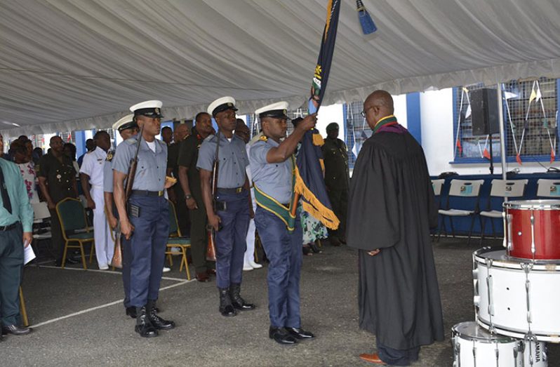 An officer presenting the Guyana Defence Force Coast Guard colours to the officiating priest