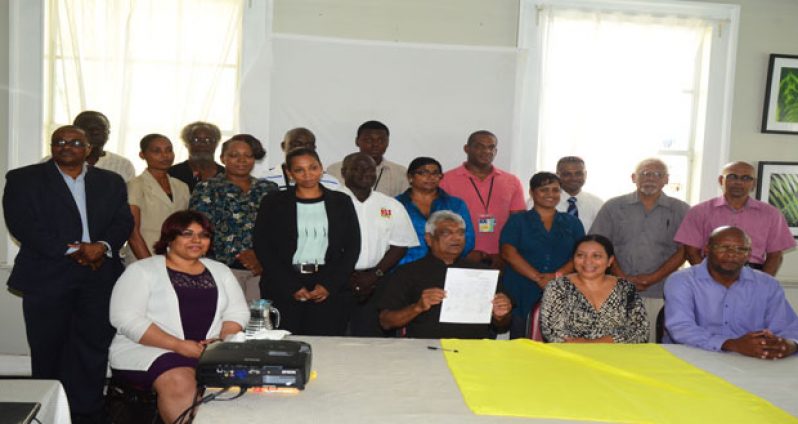 GECOM Chairman Dr Steve Surujbally (holding up documeent) Facilitator Dr Paloma Mohamed (2nd from Right) and representatives of the Media houses who were present at the Signing of the MCC