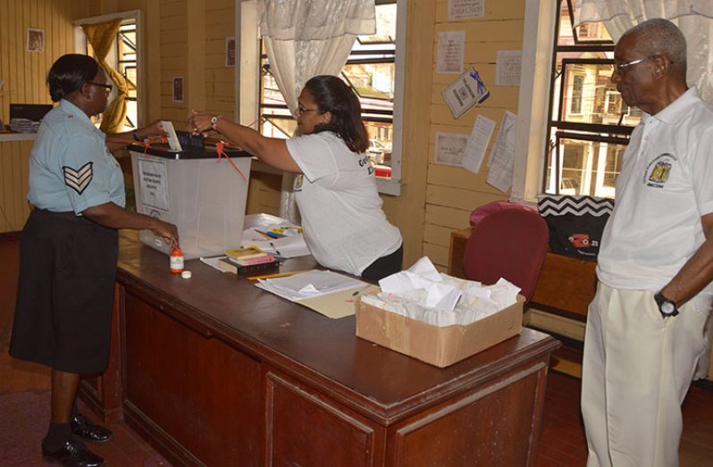 A policewoman casts her ballot at the Brickdam Police
Station under the watchful eyes of GECOM Chairman
Justice (Rtd) James Patterson (right) (Adrian Narine
photo)