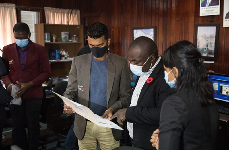 Minister of Public Affairs within the Office of the Prime Minister, Kwame McCoy and GNBA staff peruse a document