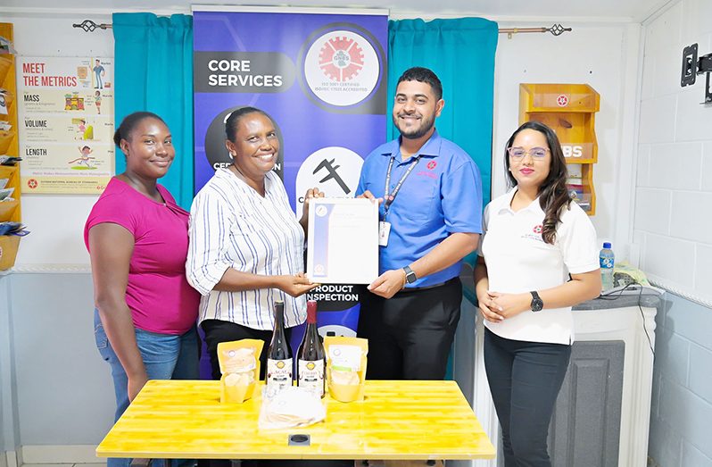 Manager of Sand Flower Products, Xuxa Lowe and Proprietress, Vanessa D’Aguiar-Lowe receive the ‘Made in Guyana’ Certificate from GNBS Technical Officer, Latchman Mootoosammi