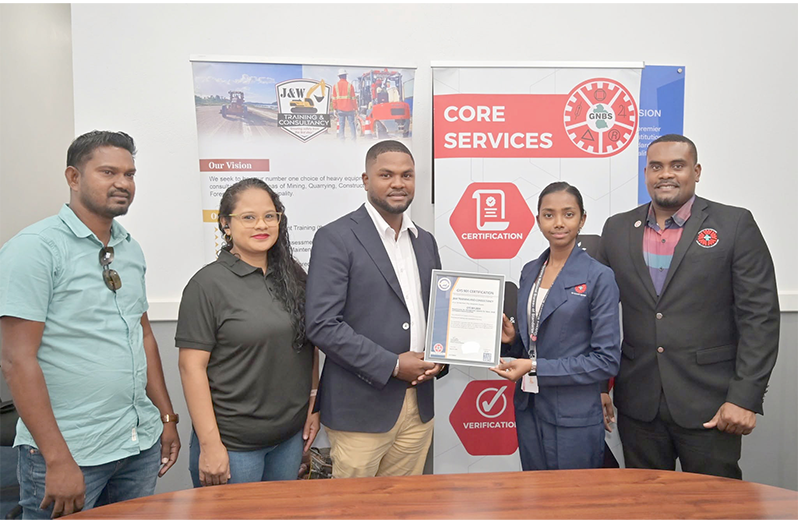 Technical Officer of GNBS, Rachel Cecil, handing over GYS 901 Certificate to Managing Director, Chavez John, flanked by GNBS Head of Certification Services, Keon Rankin and others