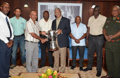 President David Granger is presented with the championship trophy by the GuyanaNRA's captain, Mr Mahendra Persaud, while members (from L-R) Mr Ryan Sampson, Mr Dylan Fields, Mr Lennox Braithwaite, Mr Terrence Stuart, Mr Paul Slowe and Brigadier General Mark Phillips look on.