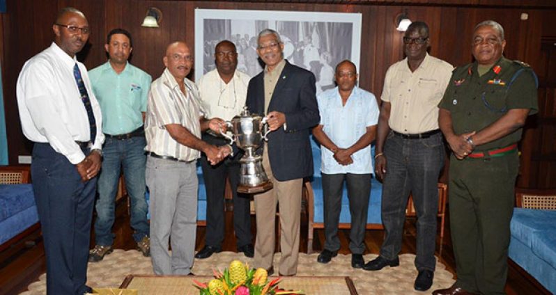 President David Granger is presented with the championship trophy by the GuyanaNRA's captain, Mr Mahendra Persaud, while members (from L-R) Mr Ryan Sampson, Mr Dylan Fields, Mr Lennox Braithwaite, Mr Terrence Stuart, Mr Paul Slowe and Brigadier General Mark Phillips look on.