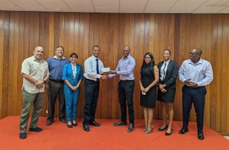 GOA President Godfrey Munroe (centre) hands over sponsorship cheque to Aubrey Hutson, flanked by Executive Members of the Guyana Olympic Association. From left: Michael Singh, Philip Fernandes, Emily Ramdhani, Aubrey Hutson, Godfrey Munroe, Vidushi Persaud-McKinnon, Cristy Campbell and Steve Ninvalle.