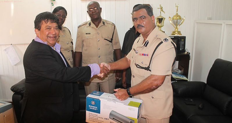 Dr. Roberto Jacgobin hands over the document laminator to Assistant Commissioner David Ramnarine while Senior Superintendent Maxine Graham; Assistant Commissioner, Operations, Christopher Griffith; and Force Chaplain Pastor Patrick Doolichand (partly hidden) look on