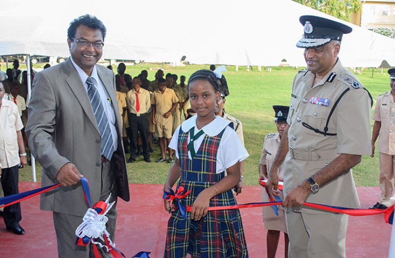 Minister of Public Security Minister, Khemraj Ramjattan (left) and Commissioner of Police, Seelall Persaud (right) assist the daughter of one of the Force’s members to cut the symbolic ribbon declaring the fitness centre open