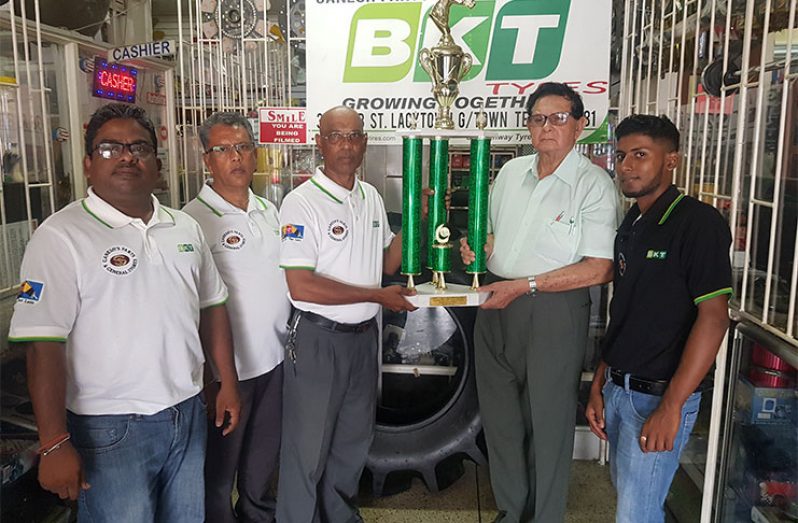 Justice Cecil Kennard, the honorary president of Kennard’s Memorial Turf Club, collects the winning trophy from sales representative of Ganesh Parts and General Store, Ron Mohammed. Proprietor Roop Persaud (second left) and other staff members also share the moment.