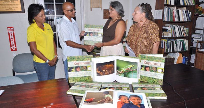 Dr. David Singh, Vice President of Conservation International, makes a donation of 12 copies of Graham Watkins’s ‘Rupununi -- rediscovering a lost world’ to the Project Manager, Gem Madhoo Nascimento. Looking on at left is Iwokrama official Ms Vanessa Benn while at right is Vanda Radzig, a supporter of the project.