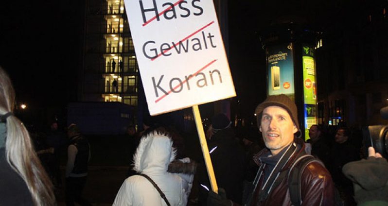 A protester holds a sign striking out the words 'hatred', 'violence', and 'Quran'. (Yermi Brenner/Al Jazeera)