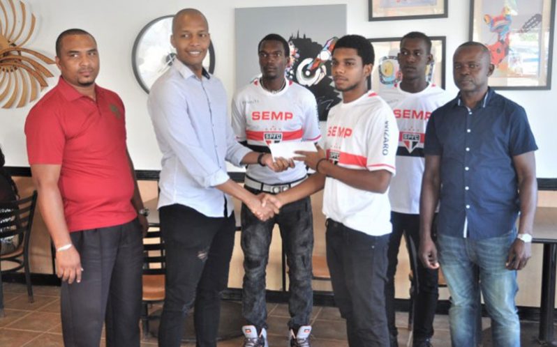 Clinton Urling of German's Restaurant presents the cheque to captain of Linden's Capital FC, Andre Myers, while Dameion Forrester and members of the club share the moment. (Photo: Sean Devers)
