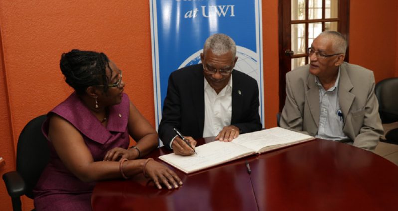 President Granger signing the Guest Book at the Institute of International Relations. He is flanked by Guyanese Dr. Mark Kirton and Trinidadian scholar Professor Rhoda Reddock
