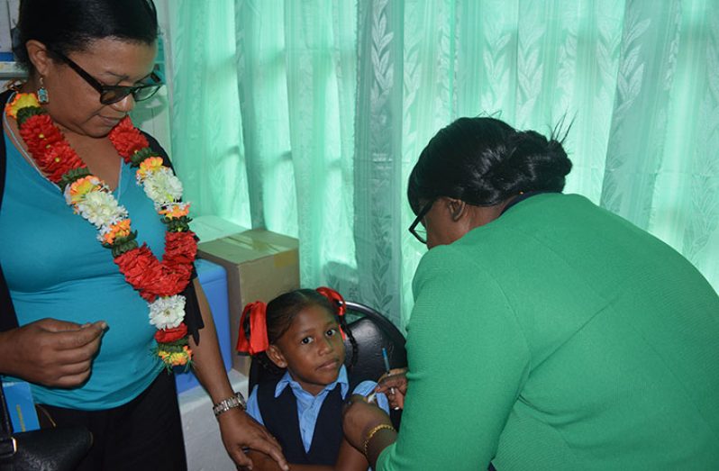 (For Page One): Minister within the Ministry of Public Health, Dr. Karen Cummings immunising the first child, a student from the Agatash Primary School, with the HPV vaccine at the Bartica Health Centre. At left is PAHO/WHO Country Office Advisor for Maternal and Child Health, Dr. Janice Woolford