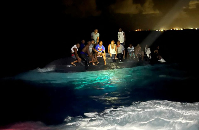 Survivors of a migrant boat that capsized perch on the overturned vessel off the coast of New Providence island, Bahamas, July 24, 2022 (Royal Bahamas Defence Force/Handout via REUTERS)