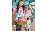 Volunteer at Humanitarian Mission Guyana Inc. hands over a food hamper to an elderly resident of Port Mourant