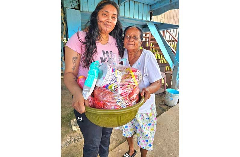 Volunteer at Humanitarian Mission Guyana Inc. hands over a food hamper to an elderly resident of Port Mourant