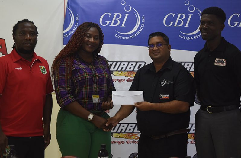 L-R GFF Youth Coach, Wayne Dover watches on as Petra’s Jackline Boodie collects the sponsorship cheque from Guyana Beverages Inc. Marketing representative, Raymond Govinda. Mark Alleyne of the Petra Organisation (at far right) watches on