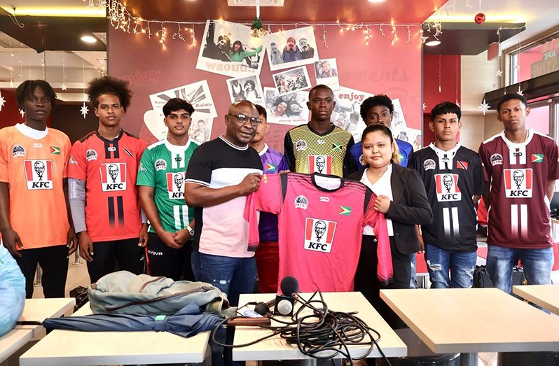 Petra representatives Troy Peters collecting kits from KFC Marketing Assistant Charmaine Farnum, with some footballers in the background