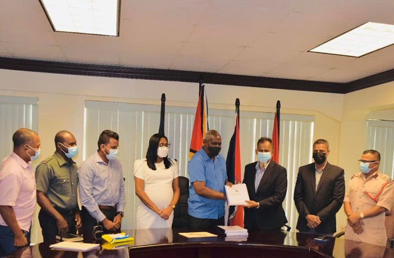 Home Affairs Minister Robeson Benn presents the signed contract to  contractor Nazeir Mohammed in the company of others