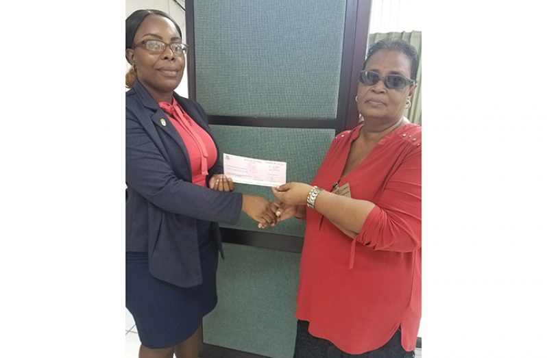 Angela Haniff receives the financial donation from a Ministry of the Presidency staff member.
