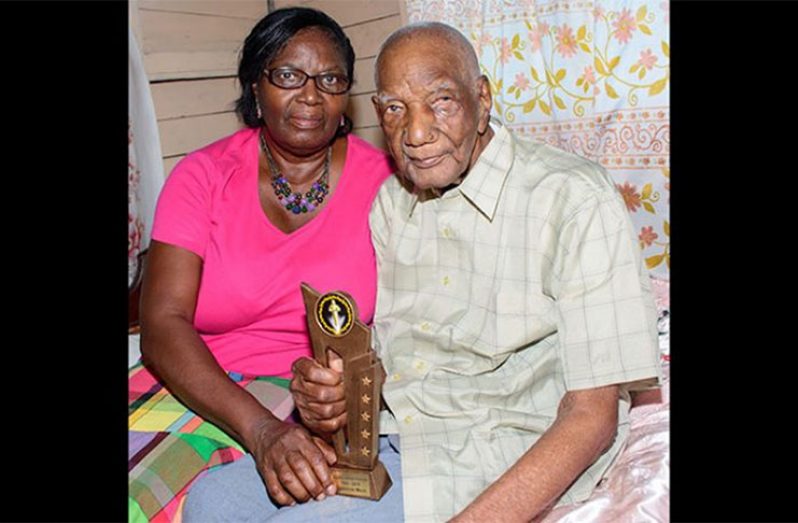 Mr. Gladstone Mack, who recently celebrated his 106th birthday. In his right hand is the award he received last year from the Government of Guyana during Independence Jubilee celebrations for being the oldest surviving man in Guyana. At left is his eldest daughter, Mrs. Winifred Camacho (Photo by Samuel Maughn)