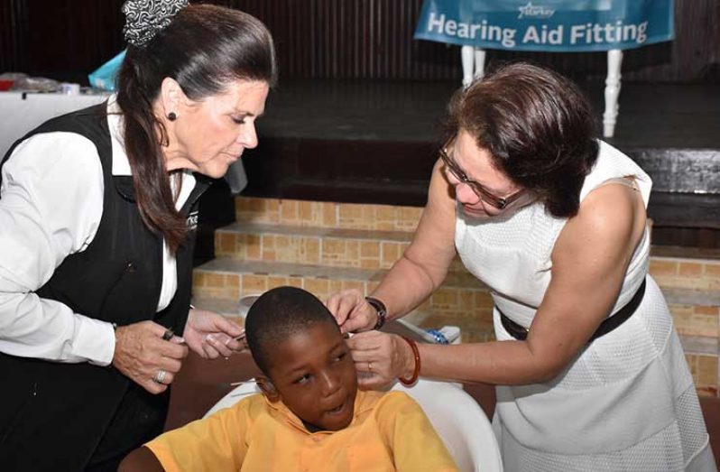 First Lady, Mrs. Sandra Granger helps Ms. Tani Austin to fit this little boy with his hearing aid, during the second phase of the Starkey hearing mission in Guyana.