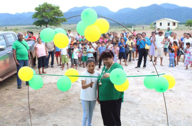 Minister of Social Protection, Hon. Amna Ally is assisted by a young girl from the community of Hiawa to cut the ribbon to officially open a multipurpose building