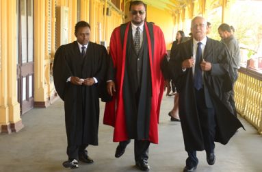 One of the many scenes from ‘Protection Games’.  Centre is city businessman, Roshan Khan, who plays the Judge Jadwah, while left is Guyana Chronicle’s Akash Persaud, who plays Prosecutor Baldeo. Right is veteran actor, Ron Robinson,  who plays the Defense Lawyer