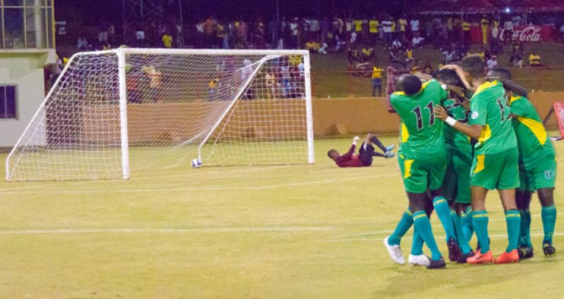 In this Samuel Maughn composite photo, Sheldon Holder (hidden) is swarmed by his teammates after scoring the second goal of the game while St Lucia goalkeeper lies beaten as the ball rolls in the net.