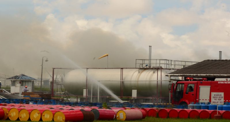 Smoke billows from this fire in the Pritipaul Singh Group of Companies’ compound, just behind these tankers, where hundreds of barrels and gas bottles containing gasoline and diesel products are stored
