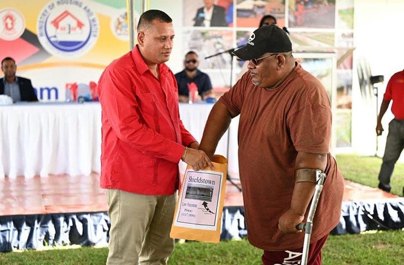 Minister of Housing and Water, Collin Croal, holds an envelope as an allottee pulls his lot number