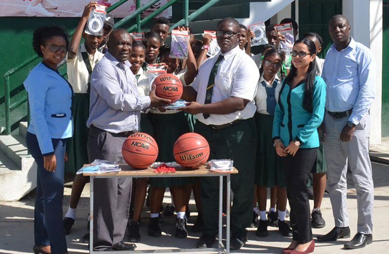 Communications Manager Troy Peters presents some of the basketballs to a teacher of the school while colleagues and students look on approvingly.