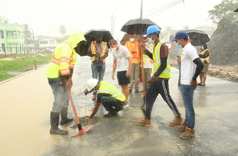 In the downpour, contractor Mark Vieira (in centre) overlooks the measurement of crush and run on the Hunter Street roadway as Minister of Public Works, Bishop Juan Edghill, looks on (Adrian Narine photo)