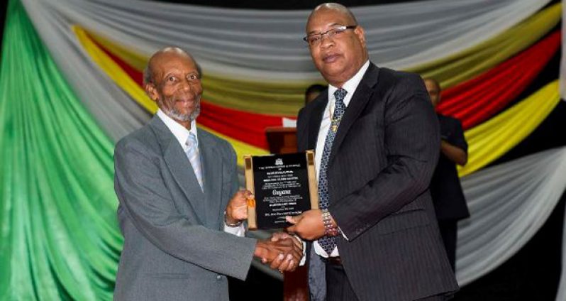 Former Governor-General of Grenada, Sir Daniel Williams, hands over the plaque of appreciation to Minister within the Ministry of Finance Juan Edghill