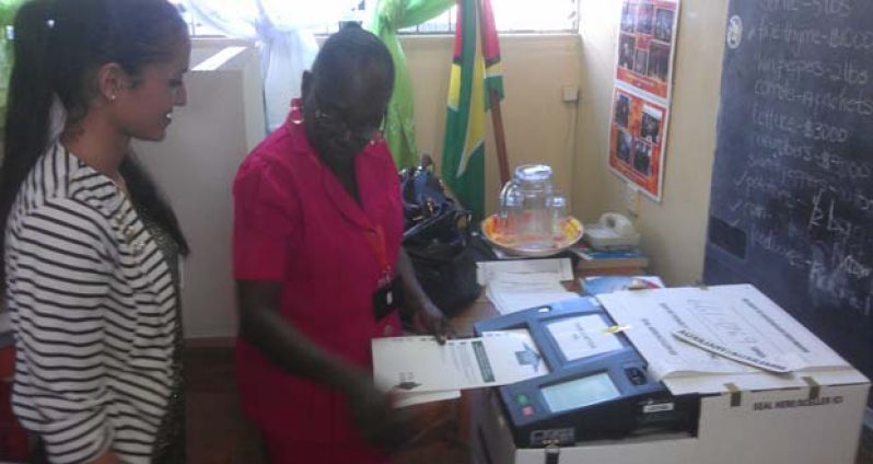 A student looks on as the Elections Coordinator inserts her ballot into the PCOS machine