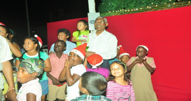 President David Granger was among scores of persons who attended last evening’s annual lighting up of the Christmas tree at Rahaman’s Park. In photo, President Granger is seen surrounded by several eager and elated children, shortly after he switched on the lights to bright up the Christmas tree