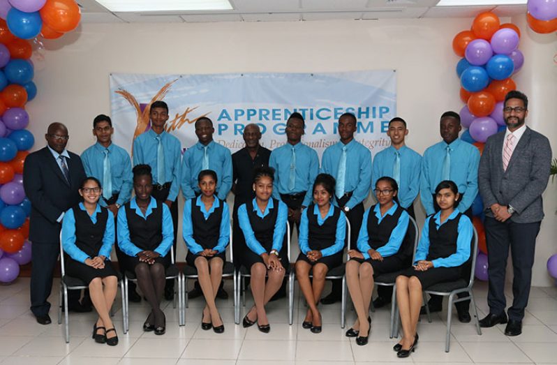 The proud batch of 14 Republic Bank Youth Link   Apprentices flanked by ACEO Education, Mr. Owen Pollard (on the left); Republic Bank Managing-Director Mr. Richard S. Sammy (at right) and Minister within the Ministry of Social Protection, Hon. Keith Scott (centre, rear)