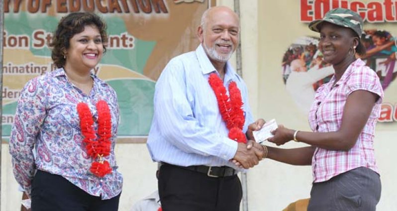 The first parent to collect the ‘Because We Care’ voucher, from President Ramotar during the launch of the initiative in Bartica yesterday Education Minister, Ms. Priya Manickchand looks on  (Sonell Nelson photo)