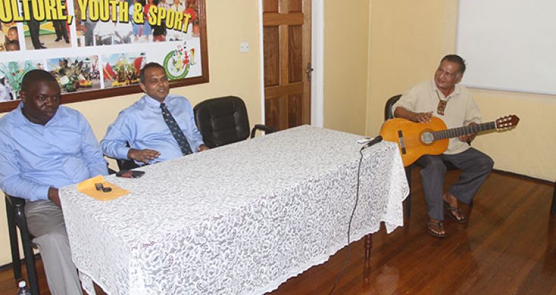 estival Coordinator Ovid Williams regales reporters with an Amerindian musical item. Looking on from left are Andrew Tyndall and Dr. Frank Anthony