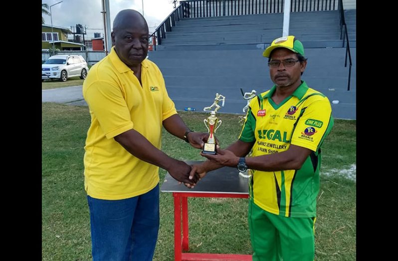 Georgetown Softball Cricket League Inc. president Ian John hands over the man-of-the-match trophy to Uniss Yusuf.