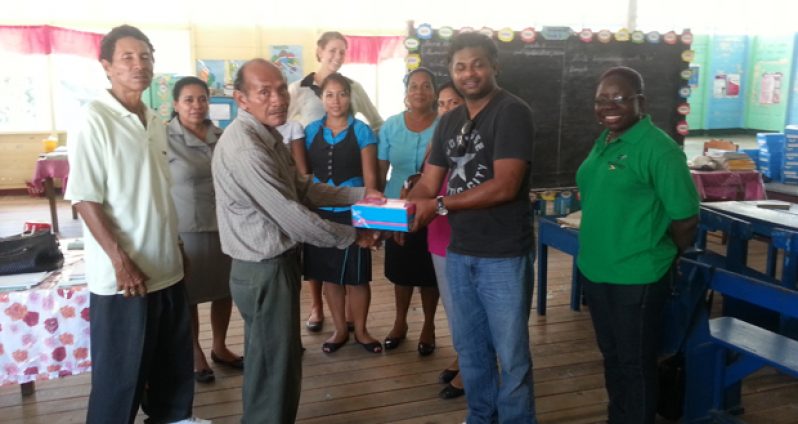 Chief Executive Officer (ag), Mr Deodat Indar along with CSR Officer, Ms Cassandra George-Mangru and Assistant Accountant, Ms Gaitrie Shivsankar handing over the footwear to Headmaster John Boyan, teachers  and the Toshao