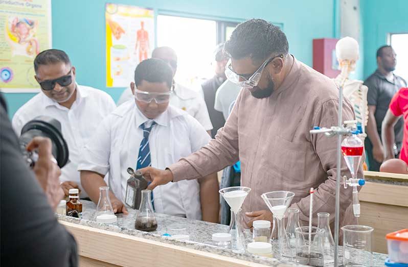 President Dr. Irfaan Ali joins a student of the Tuschen Secondary School for an experiment (Delano Williams photo)
