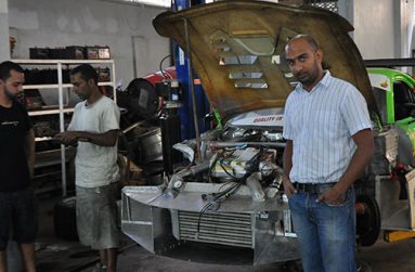 Irfaan Kalamadeen poses next to his Mazda RX7 while ace tuner Omar Crespo (first from left) ponders his next installation