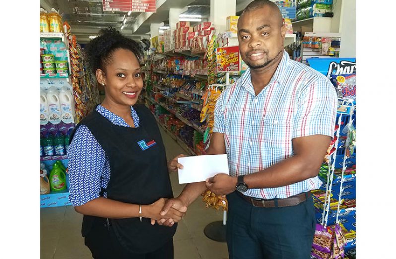 Supervisor at Andrews Supermarket, Stacy Burnett (left) hands over the sponsorship to Edison Jefford at the entity's Aubrey Barker Road, South Ruimveldt Gardens location.